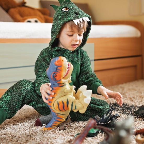 Barn i grøn dinosaurdragt leger med dinosaurfigurer på gulvet.